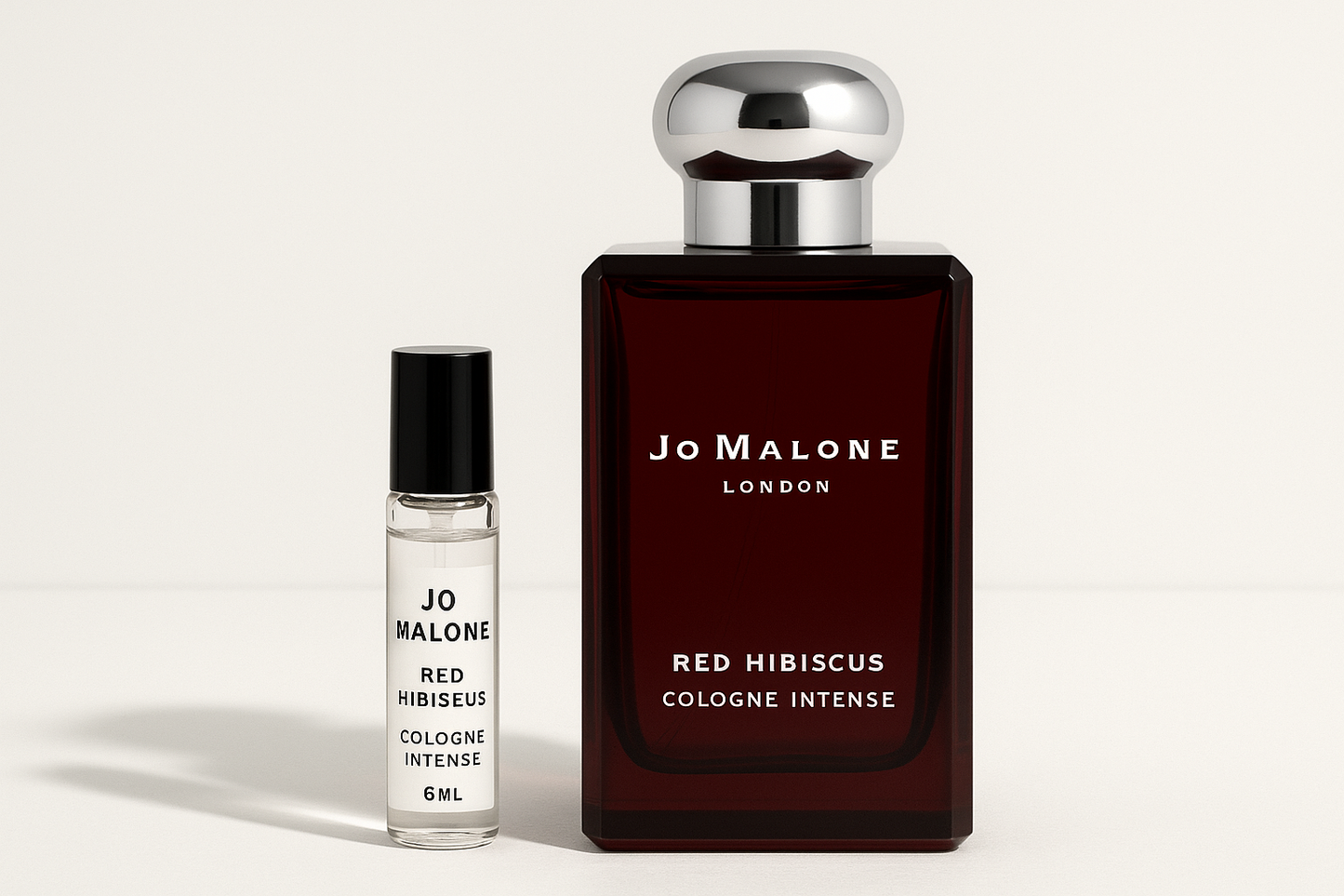 Eine 6-ml-Probe von Jo Malone Red Hibiscus Cologne Intense steht neben einer 100-ml-Parfümflasche von Jo Malone Red Hibiscus Cologne Intense, die eine weiße Schrift auf einer dunkelroten Flasche hat